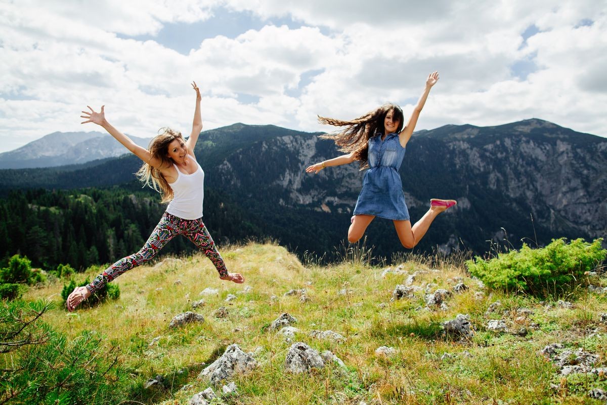 two long hair girls happy jump in mountains with exciting view of Montenegro