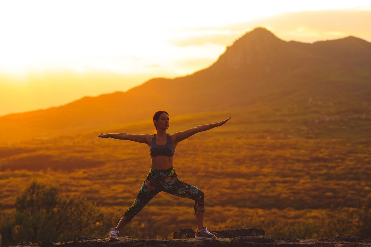 Silhouette of young woman practicing yoga or pilates at sunset or sunrise in beautiful mountain location